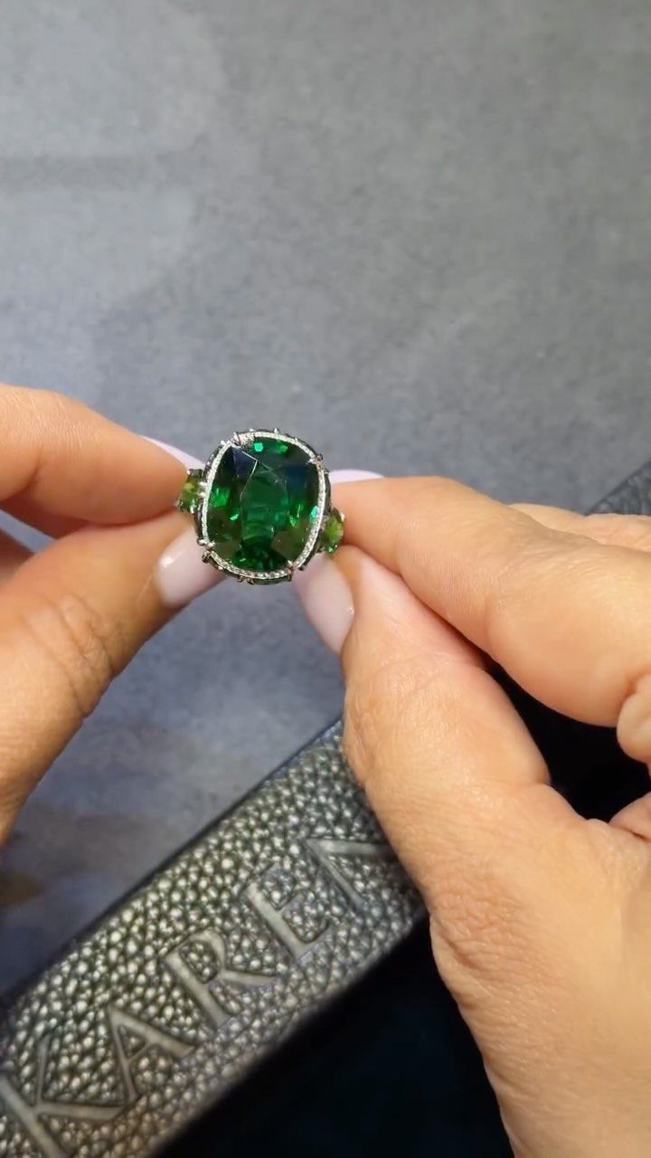 Silver ring with a large green gemstone held by two hands