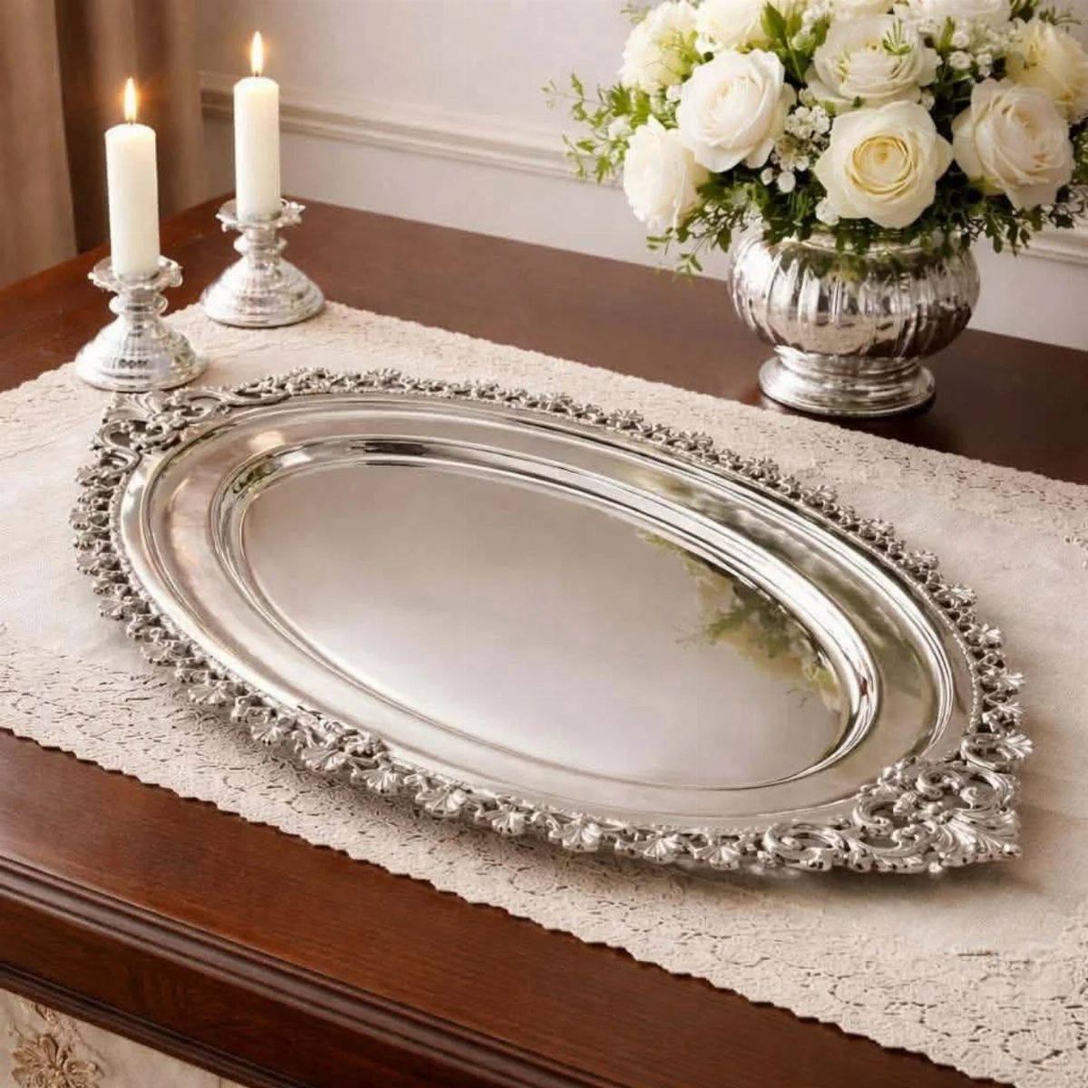 Ornate oval silver serving tray on a lace runner with white roses.