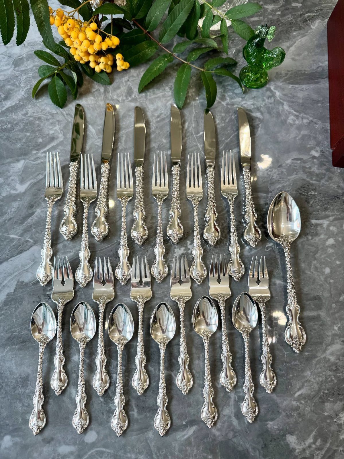 Ornate silver cutlery set arranged on a grey marble surface with yellow flowers.