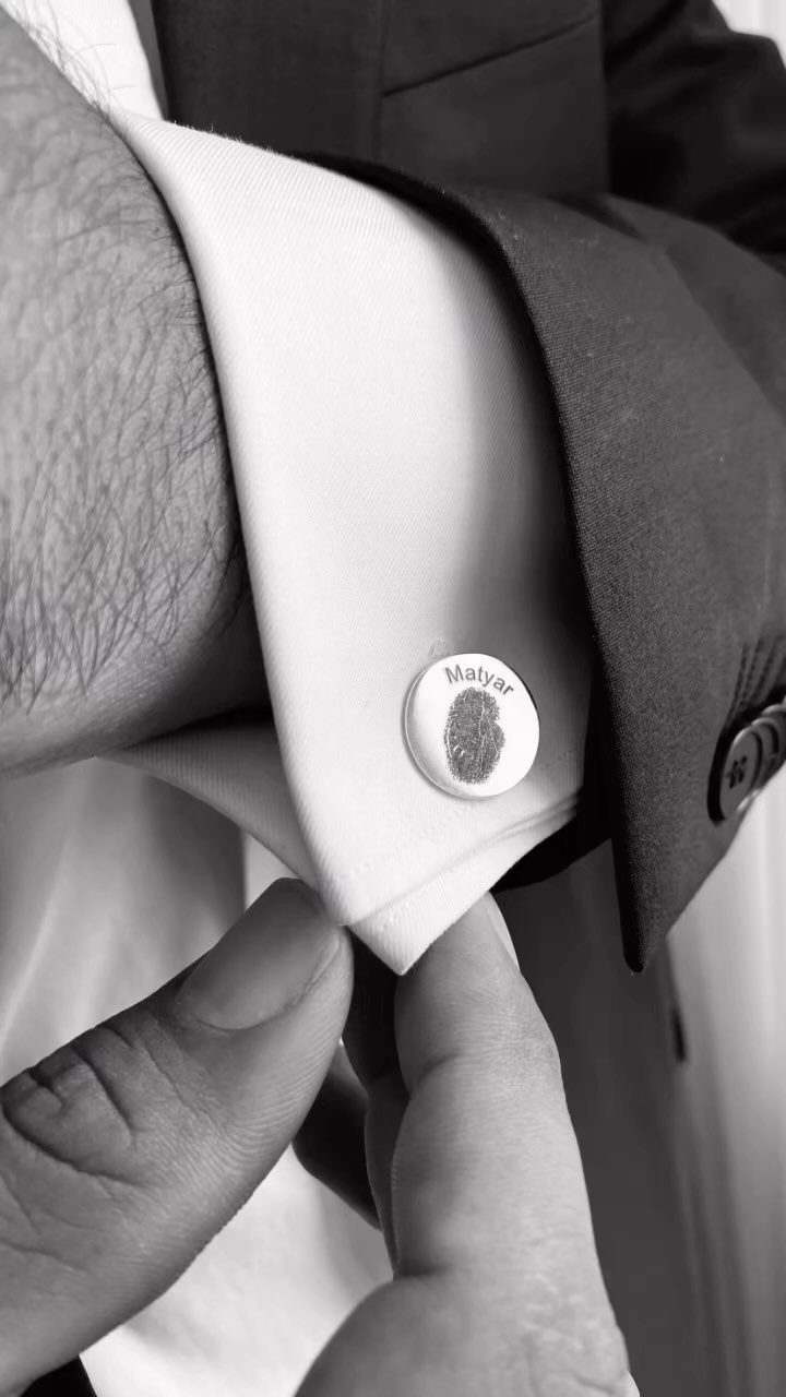 Silver cufflink with a fingerprint and name on a white shirt cuff.