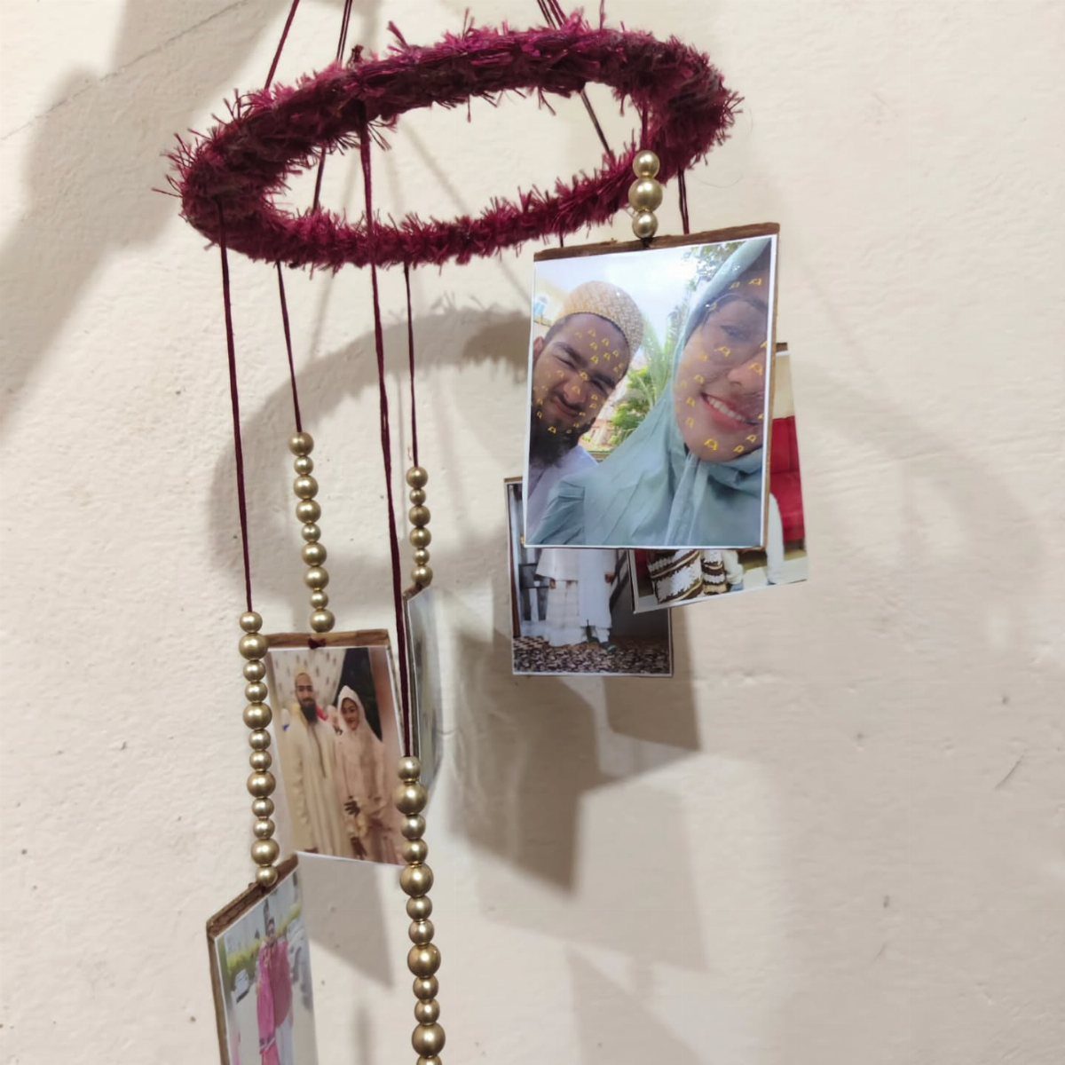 Handmade photo mobile with a burgundy hoop and gold beads hanging against a wall
