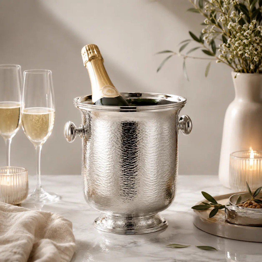 Hammered silver champagne bucket with a bottle and two glasses on marble.