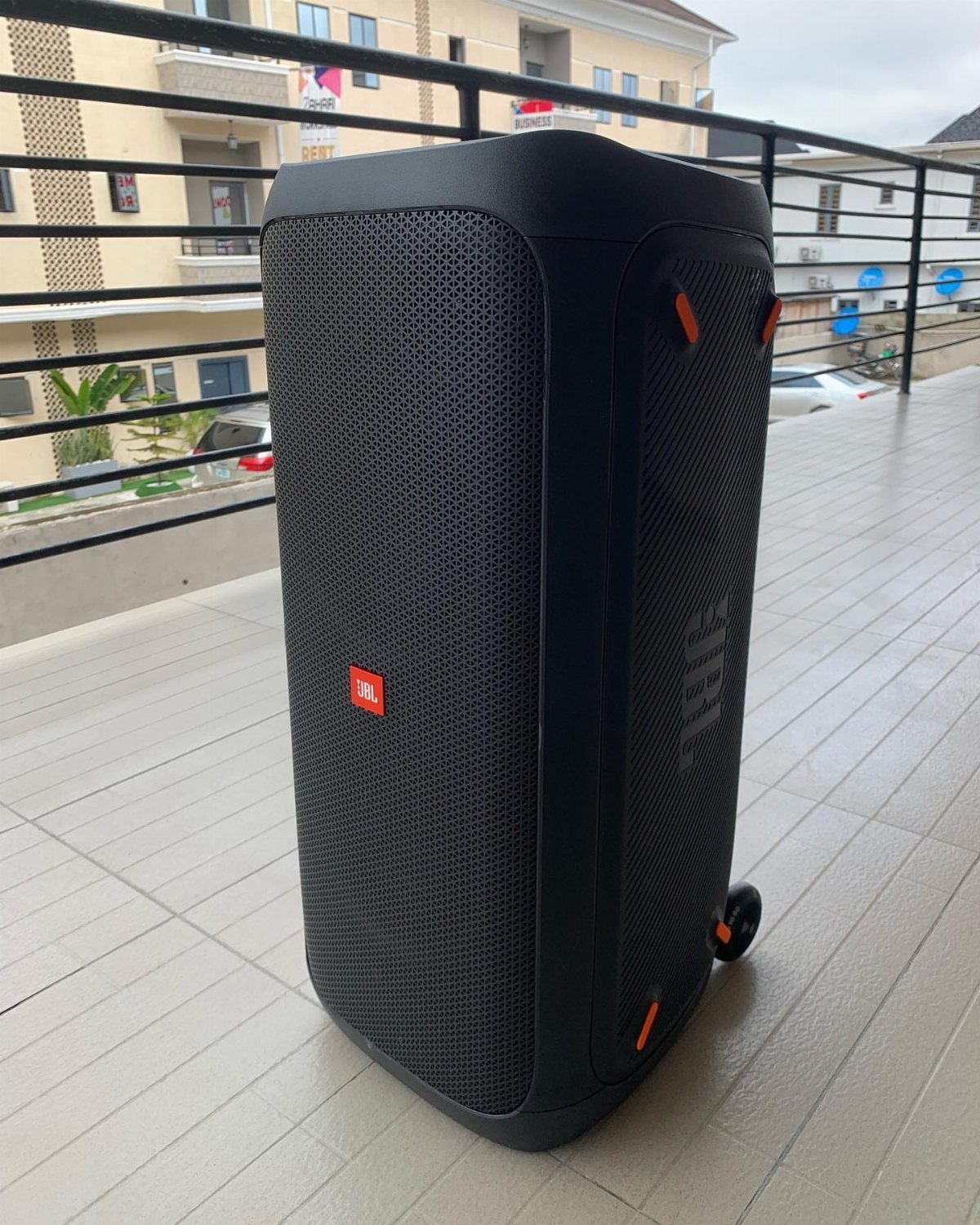 Large black JBL party speaker standing on a tiled balcony with metal railings.