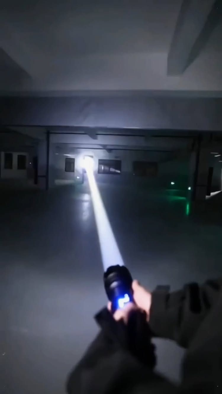 Powerful black flashlight emitting a bright white beam in a dark concrete garage