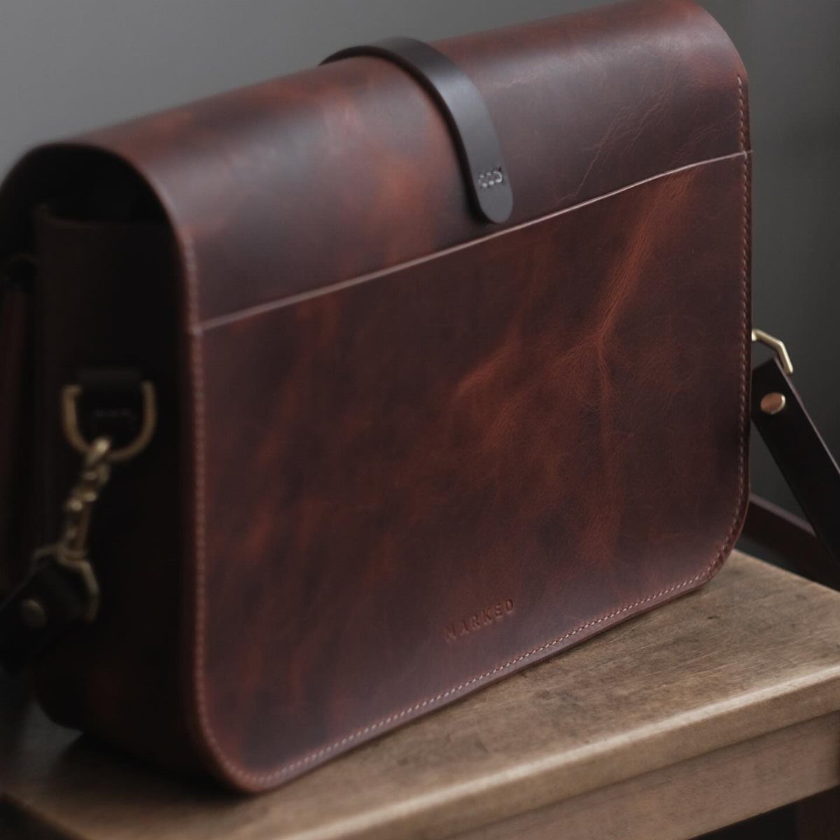 Brown leather messenger bag sitting on a light wooden shelf.