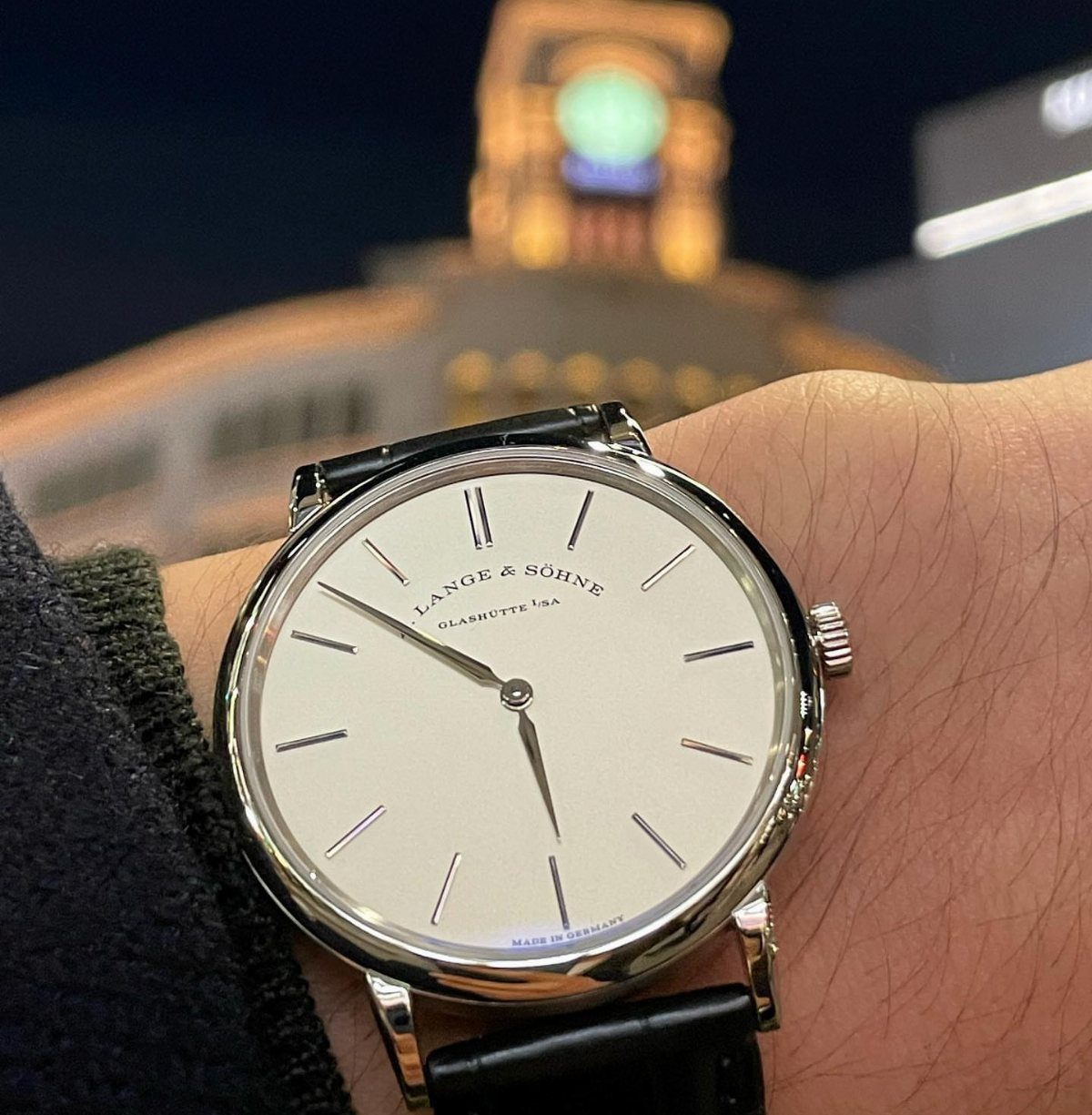 Silver wrist watch with white face and black leather strap on a wrist