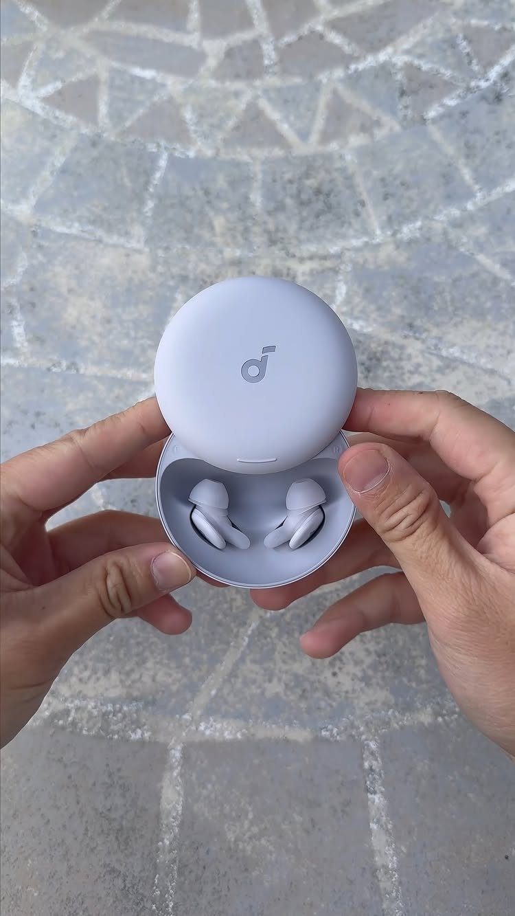 White wireless earbuds in an open charging case held by two hands.
