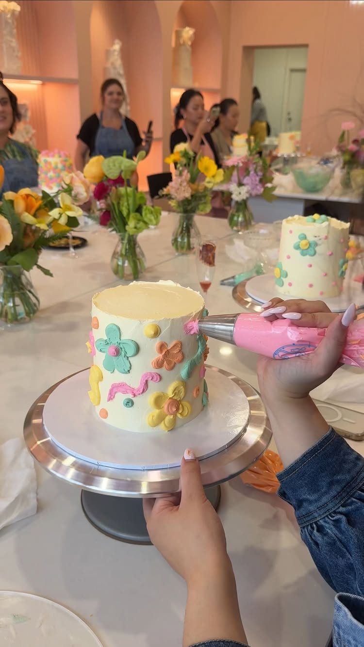 Hands decorating a white cake with colorful frosting in a bright studio setting