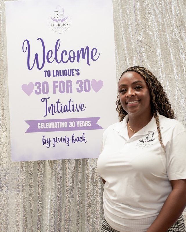 Woman smiling next to a sign for a 30th anniversary charity giving back initiative.