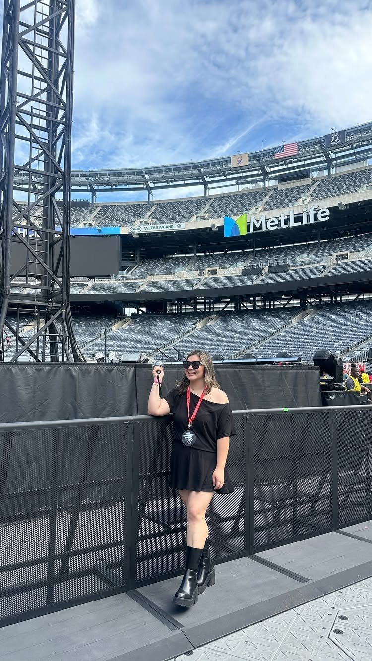 Woman in black dress posing at a large stadium concert venue.
