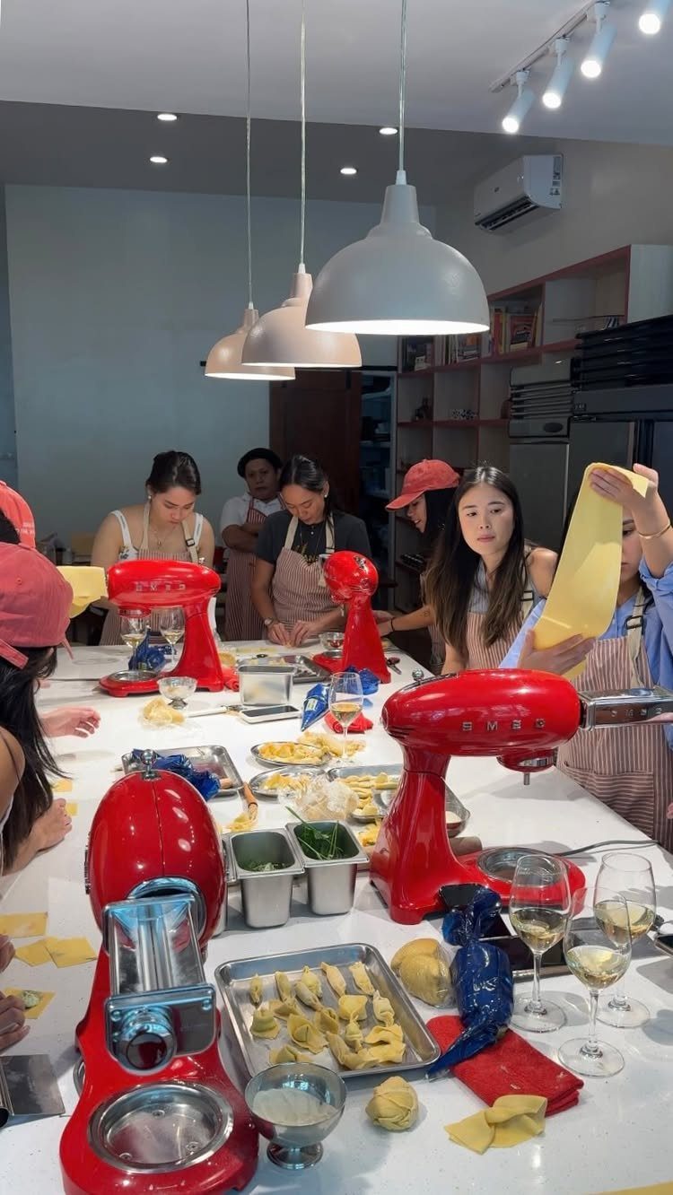 Women in aprons making fresh pasta with red stand mixers in a kitchen.
