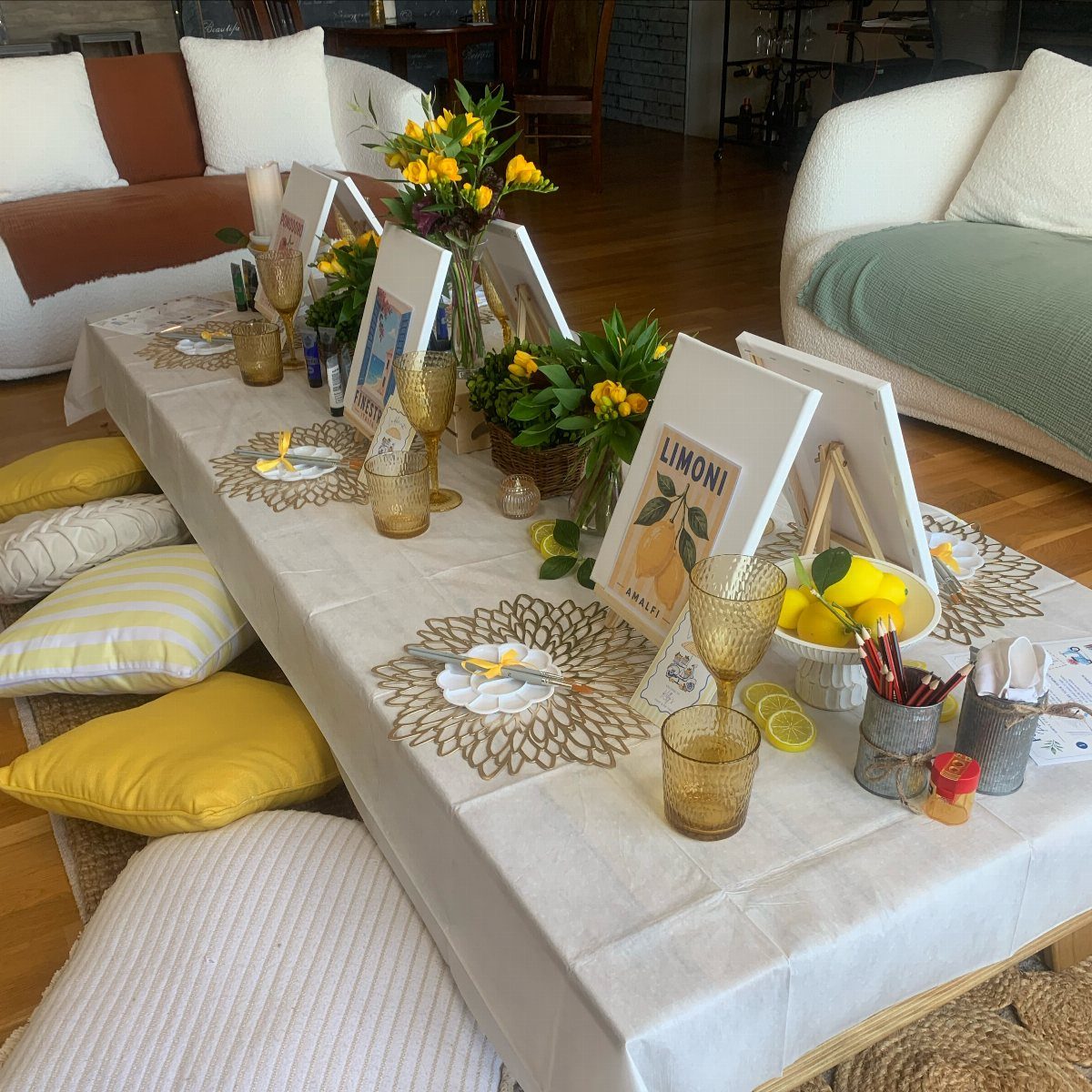 Low white table decorated with yellow flowers, gold glasses, and small framed art.