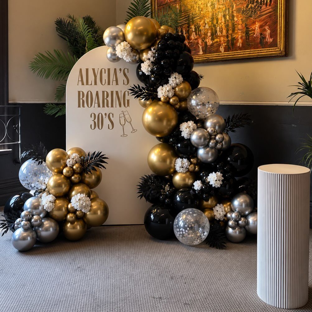Roaring 30s birthday backdrop with gold, black, and silver balloon garlands and text.