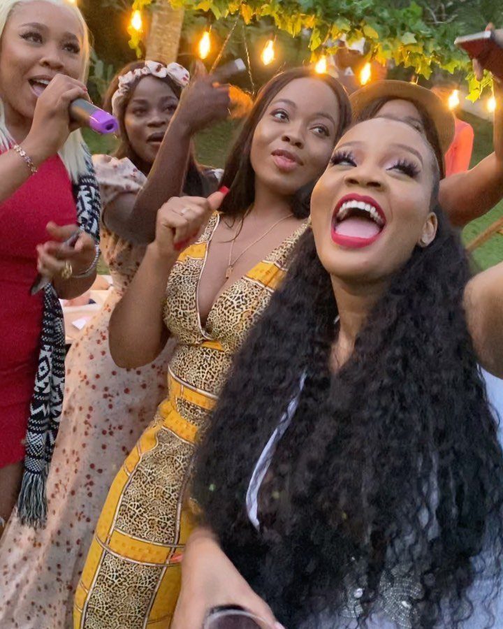 Group of women singing into microphones outdoors under warm string lights at night.