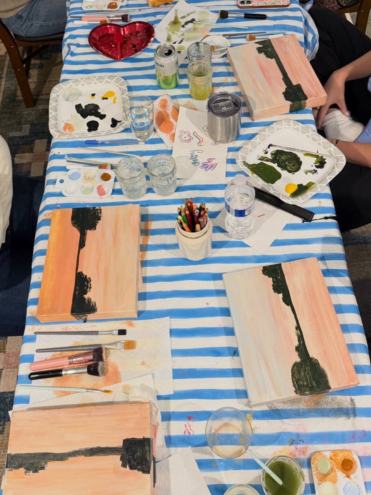 Art supplies and abstract paintings on a blue and white striped table cloth