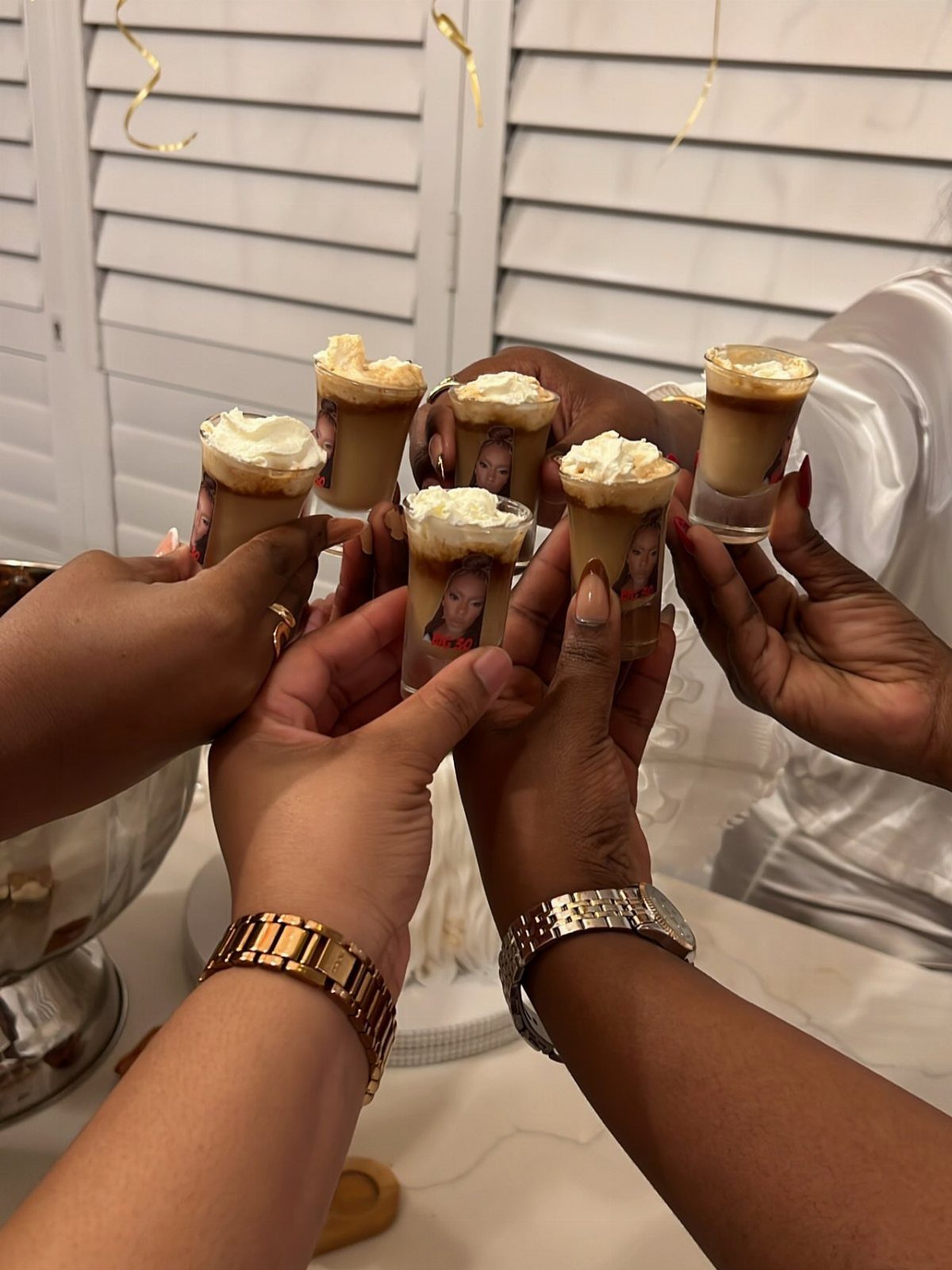 Hands holding dessert shooters with personalized photo labels for a birthday celebration.