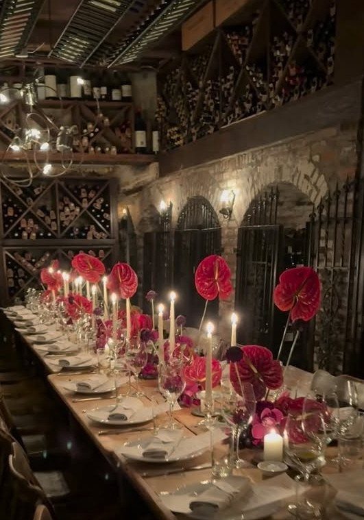 Long dining table with red flowers and candles in a rustic wine cellar