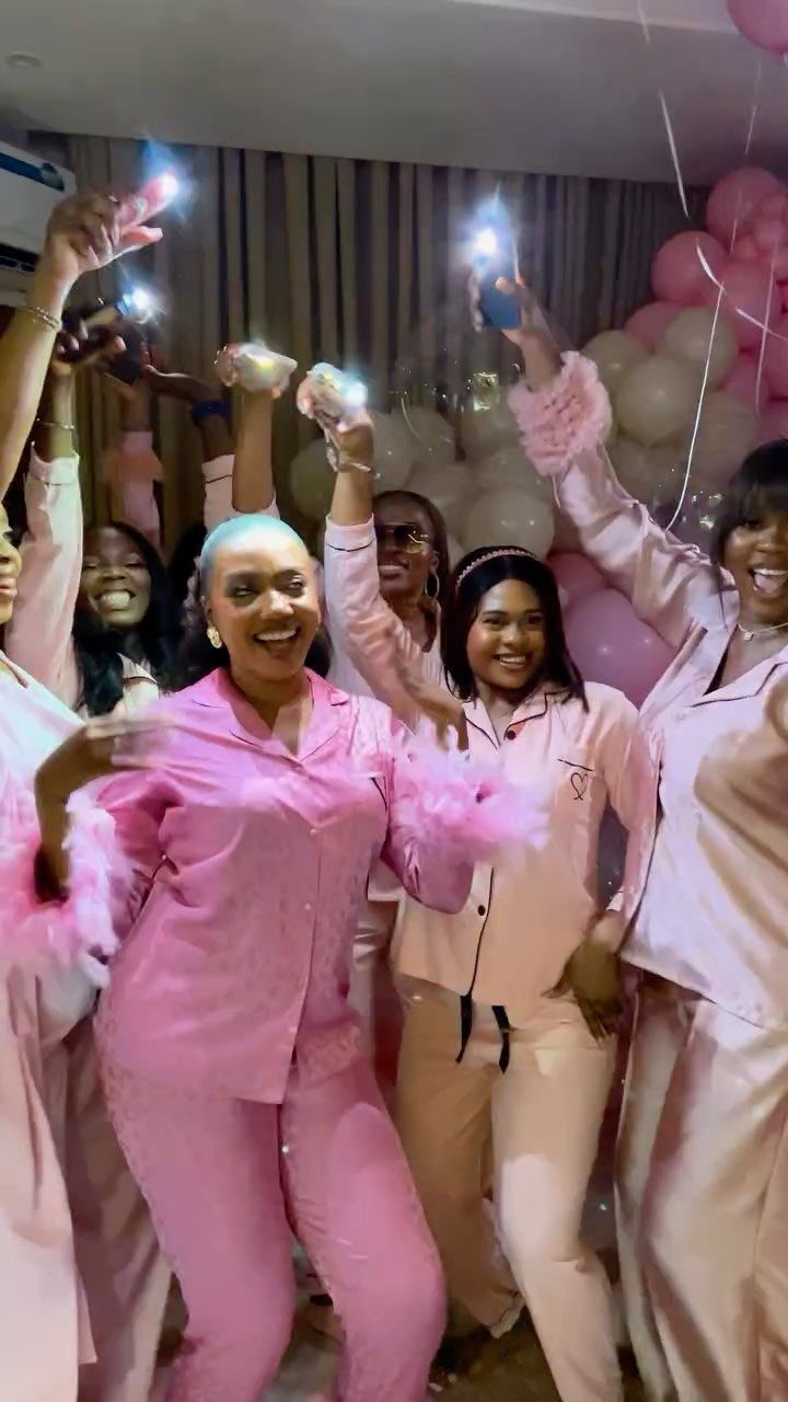 Women in pink satin pajamas cheering with glowing lights and pink balloons.