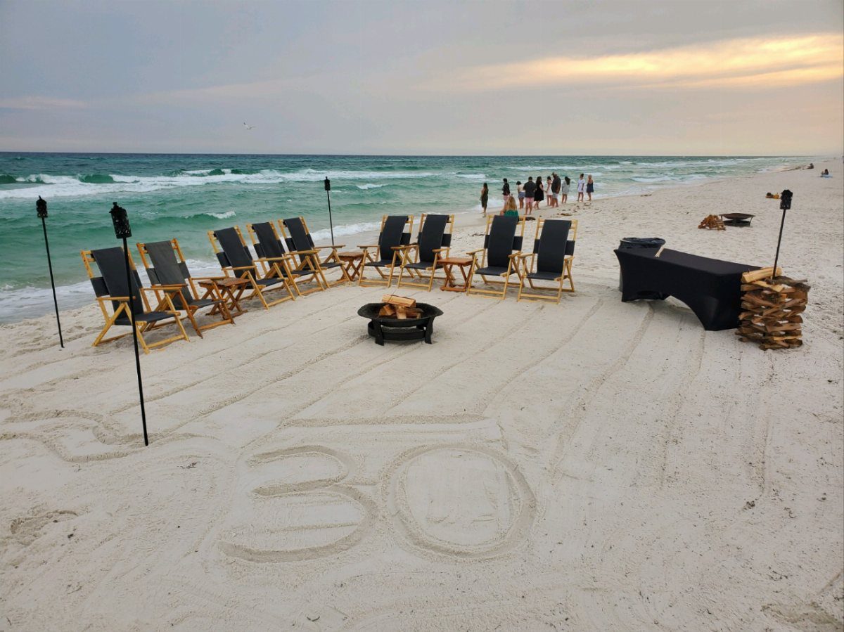 Beach bonfire setup with lounge chairs and the number 30 drawn in sand.