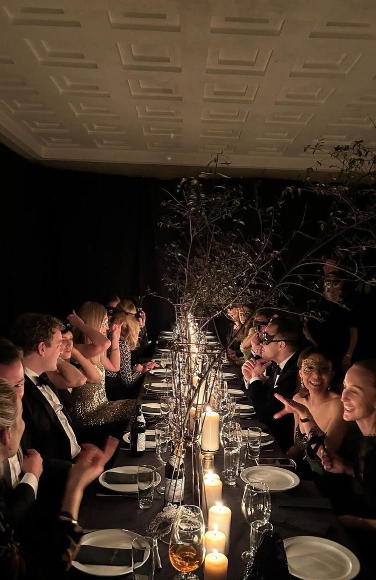 Formal dinner party with guests in black-tie attire seated at a candlelit table.
