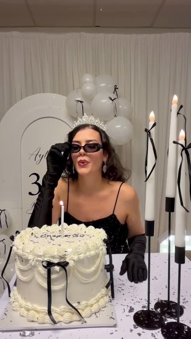 Woman in tiara and black gloves celebrating with a white themed birthday cake
