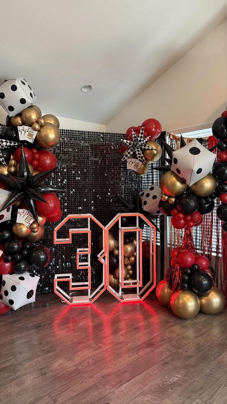 Red neon 30 sign surrounded by black, gold, and red balloons with giant dice.