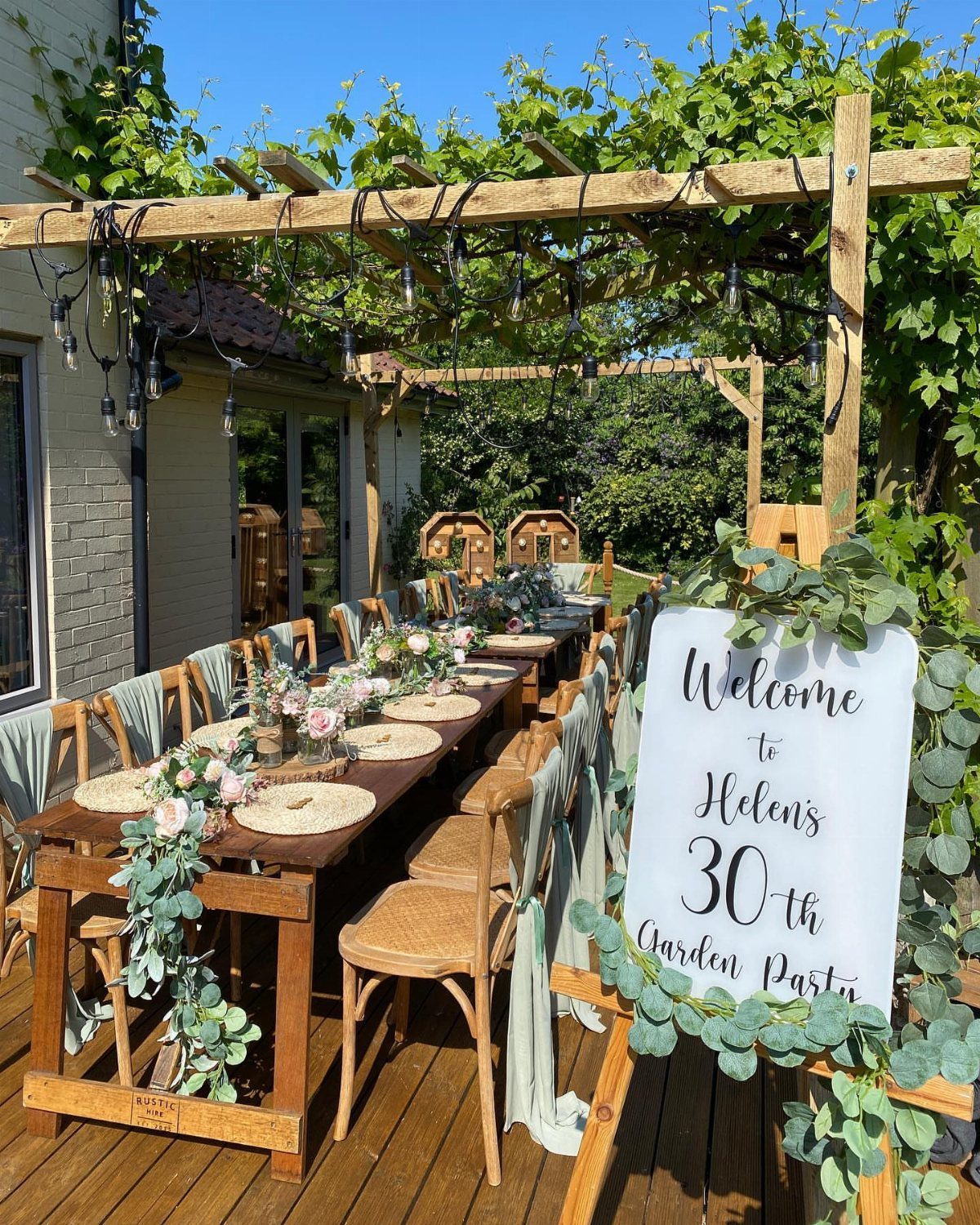 Outdoor wooden dining table set for a 30th garden party under a pergola.