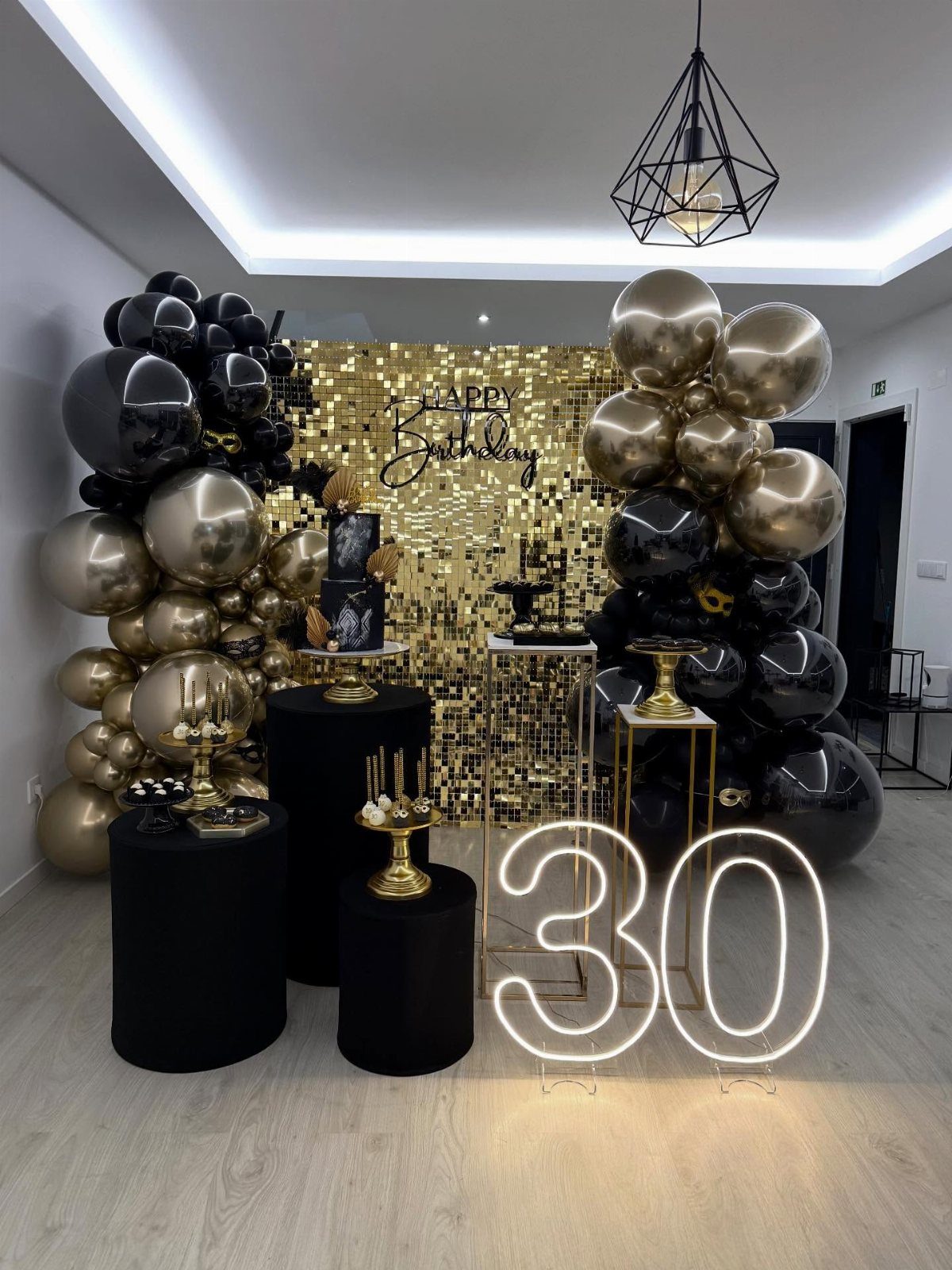 Gold and black birthday decorations with a large neon 30 sign and balloons.