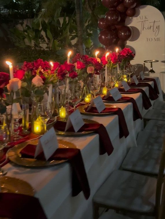 Elegant dinner table setting with red roses, gold plates, and 30th birthday signage.