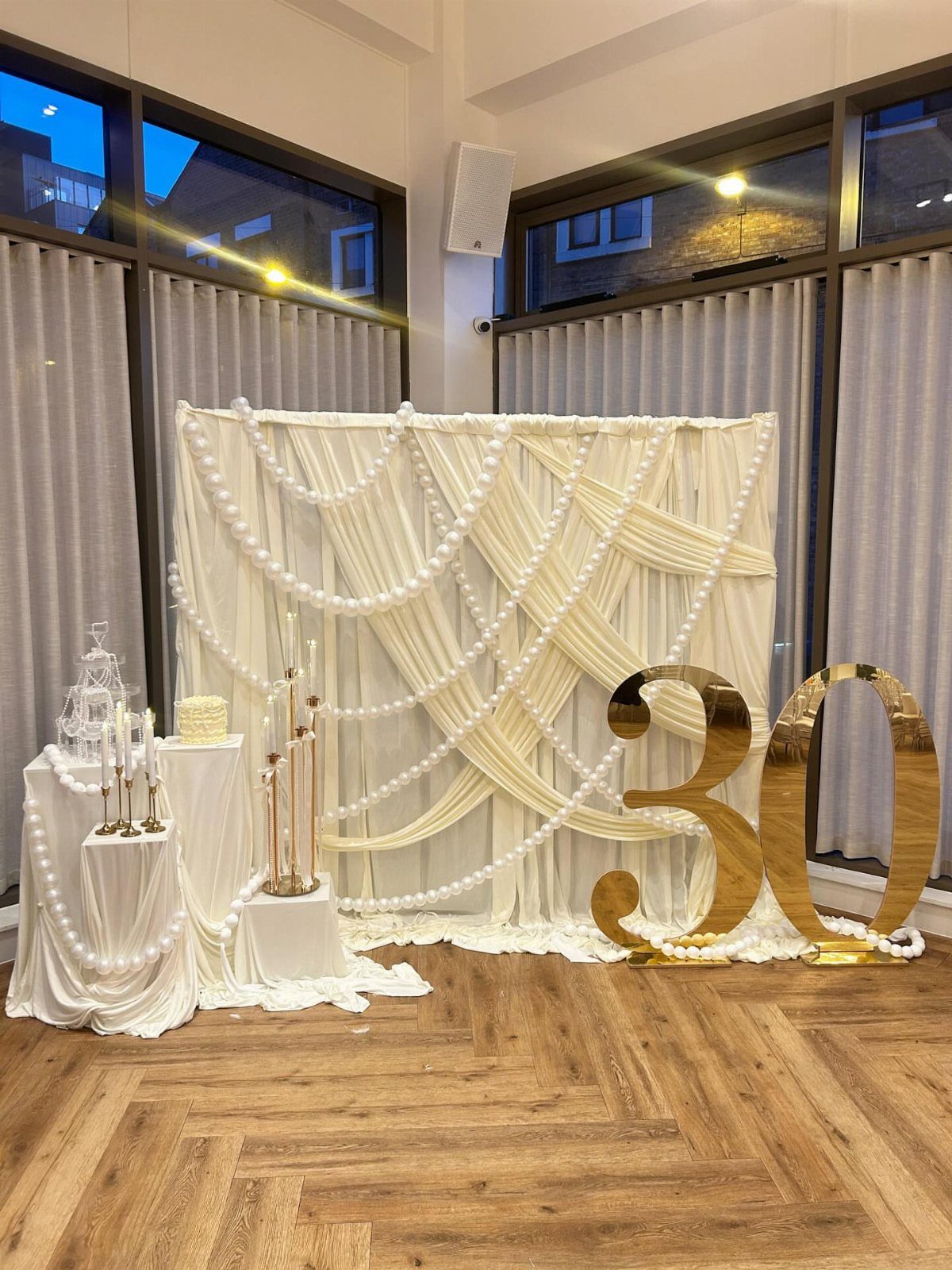 White draped backdrop with pearls and large gold 30 numbers for a birthday.