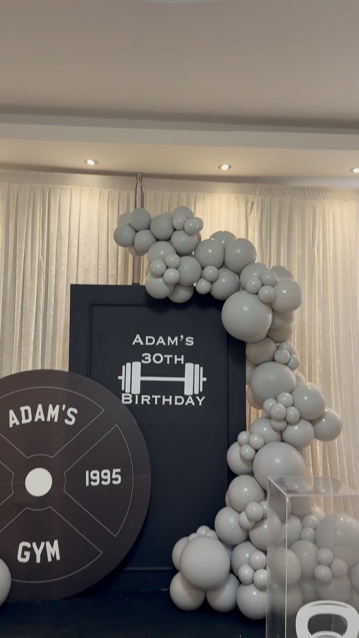 Gym themed 30th birthday decoration with black backdrop, weight plate, and grey balloons.