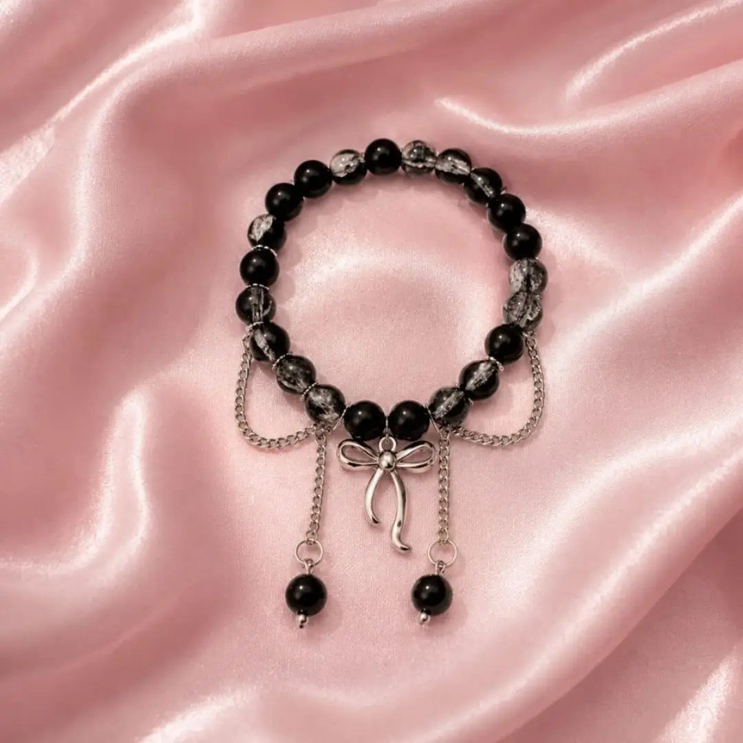 Beaded bracelet with black stones and silver bow charm on pink satin fabric