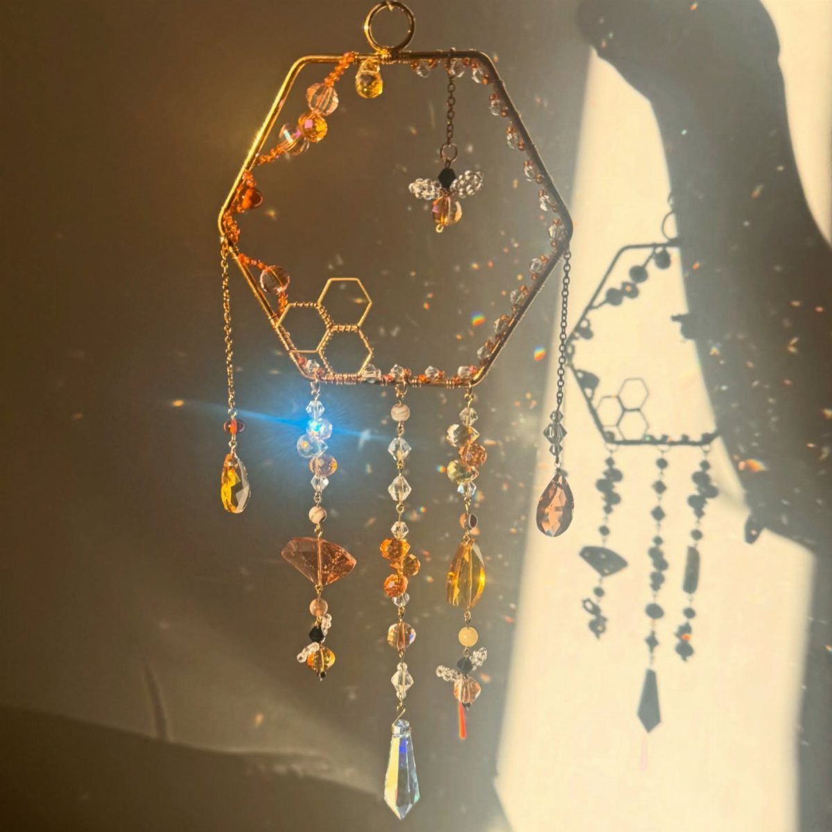 Hexagonal crystal suncatcher with amber beads and a bee charm casting rainbow light.