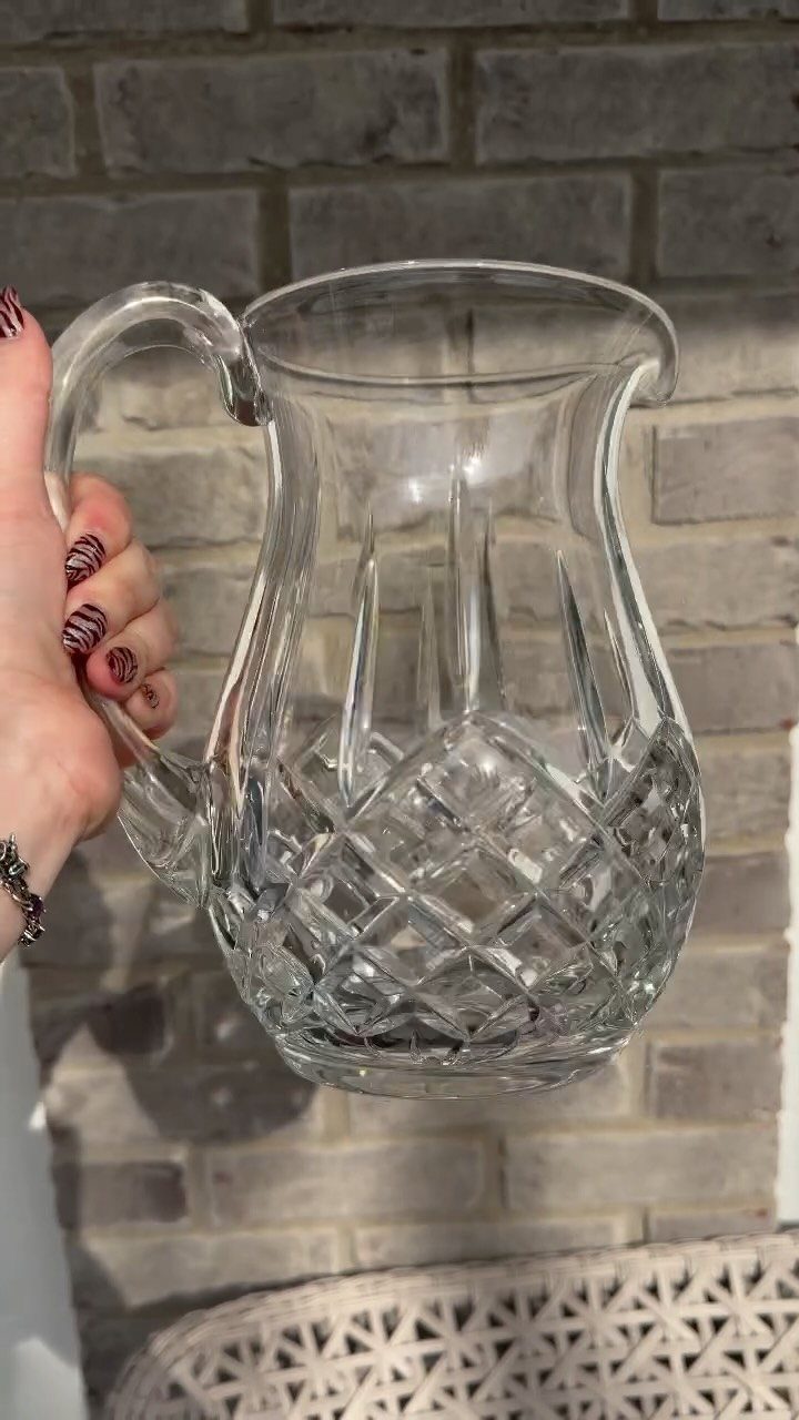 Cut-glass pitcher with diamond patterns held by a hand against a brick wall.