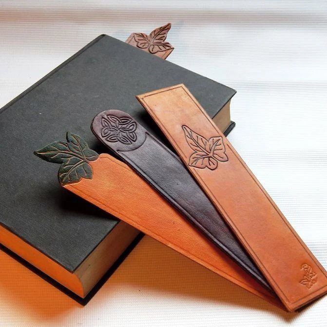 Leather bookmarks with embossed leaf designs resting on a dark hardcover book.