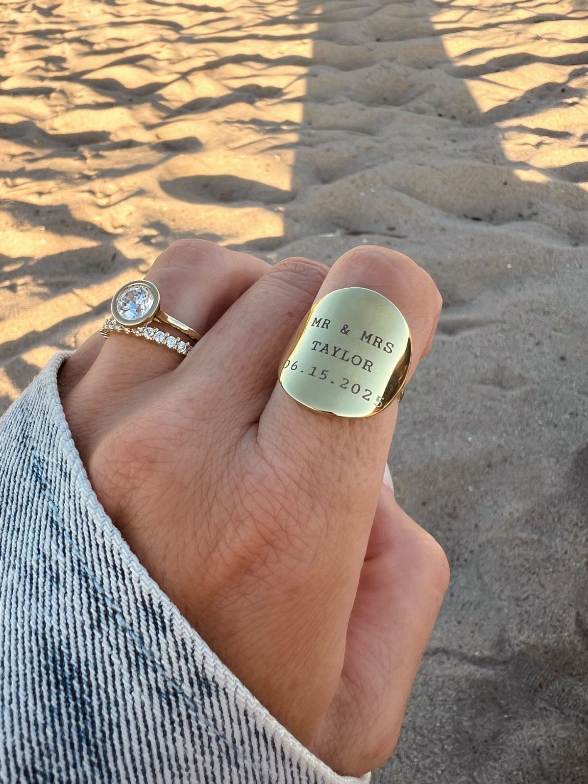 Engraved gold signet ring and diamond engagement ring on a hand at the beach