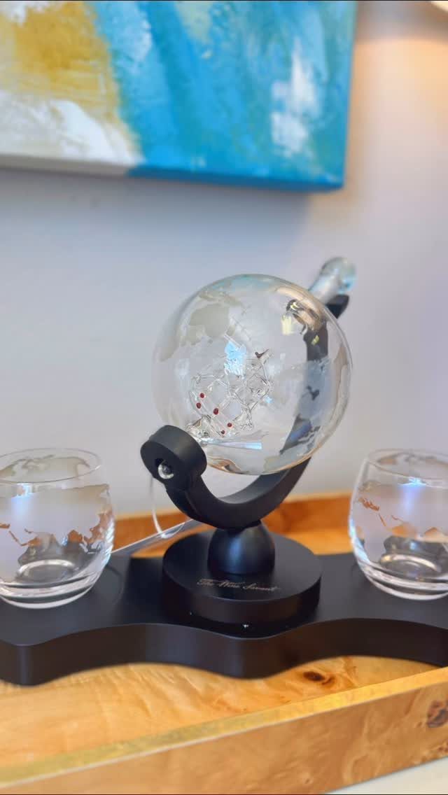 Globe decanter with ship inside and two glasses on a black stand.