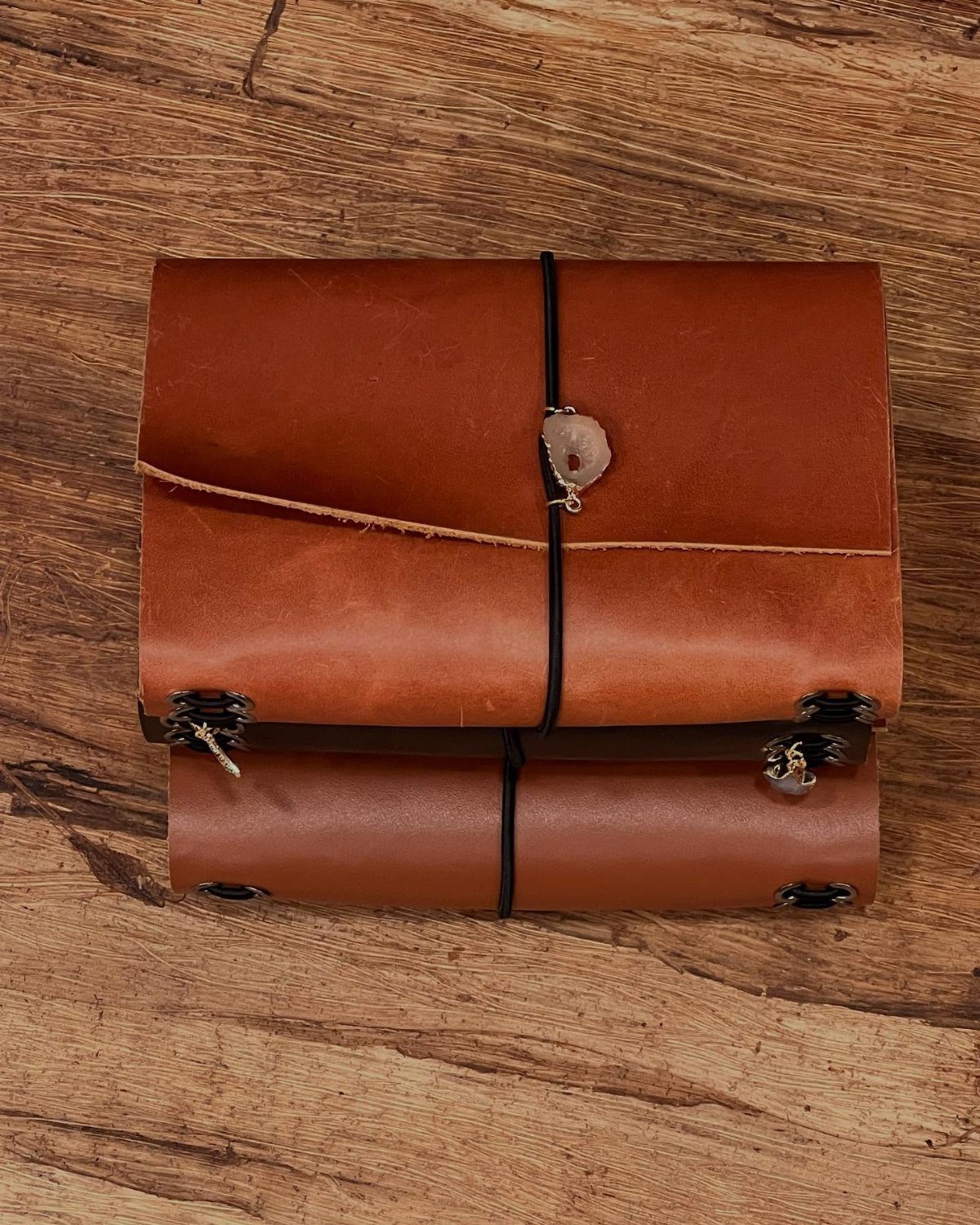 Brown leather-bound journal with a crystal charm on a rustic wooden background.