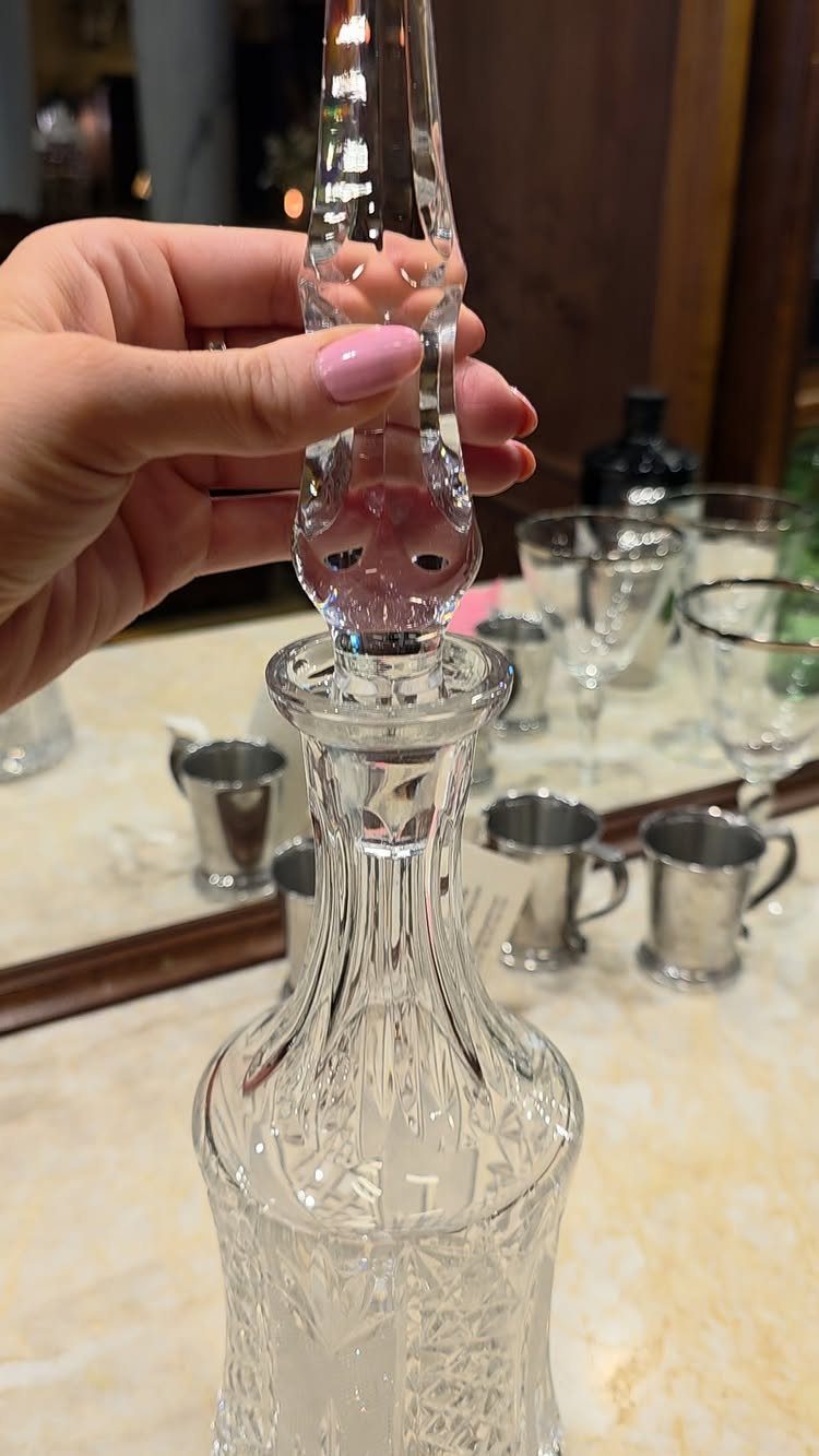 Crystal decanter with an ornate stopper held by a hand with pink nails.