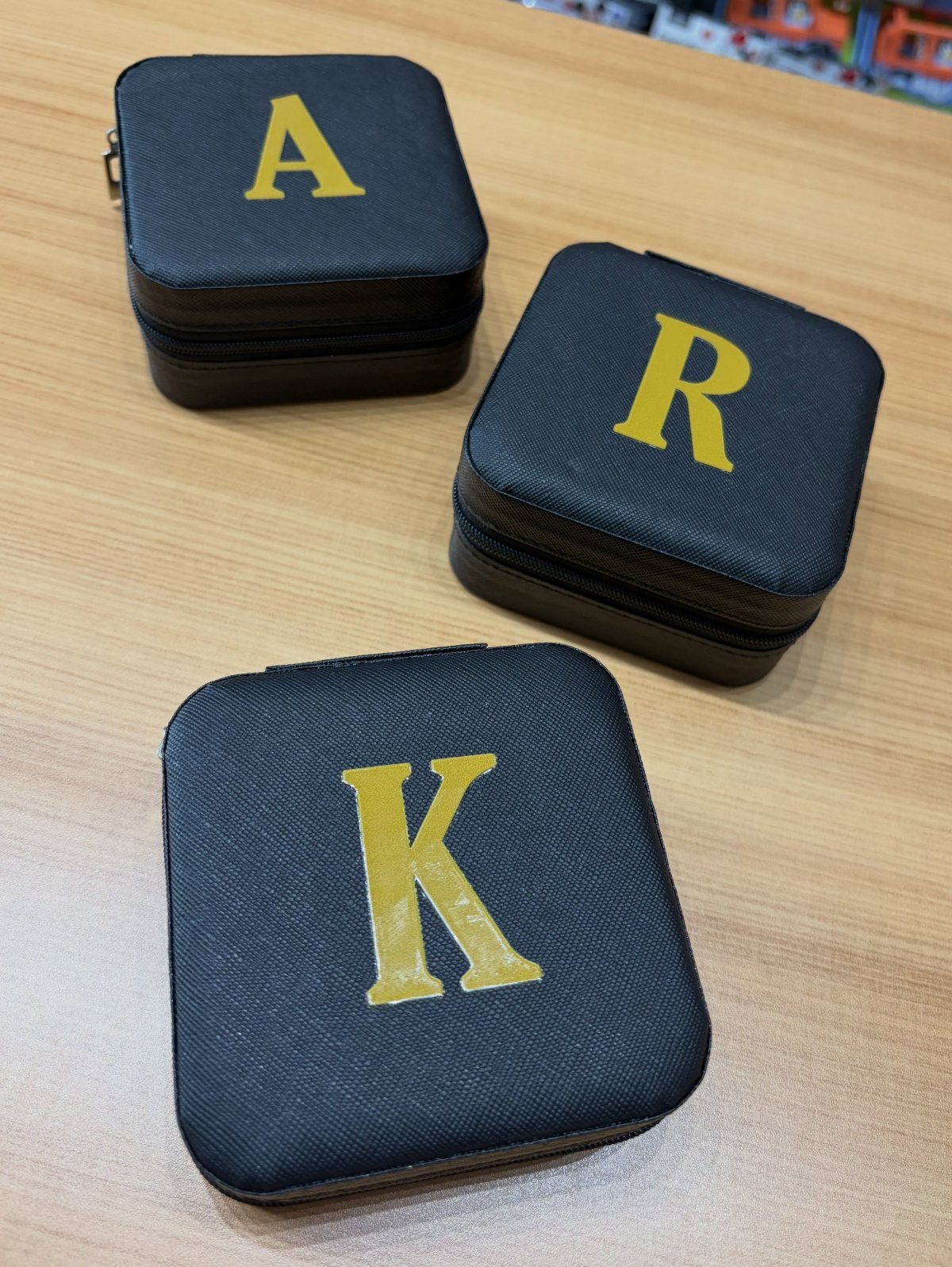 Three black leather jewelry cases with gold embossed initials on a wooden table.
