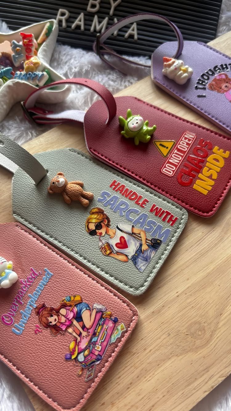 Colorful leather luggage tags with cartoon graphics and charms on a wooden board.