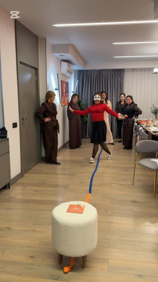 Blindfolded woman balancing on a blue line while friends watch during a party game.
