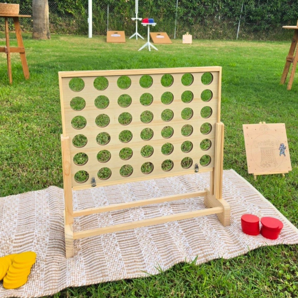 Giant wooden Connect Four game on a striped blanket in a grassy yard