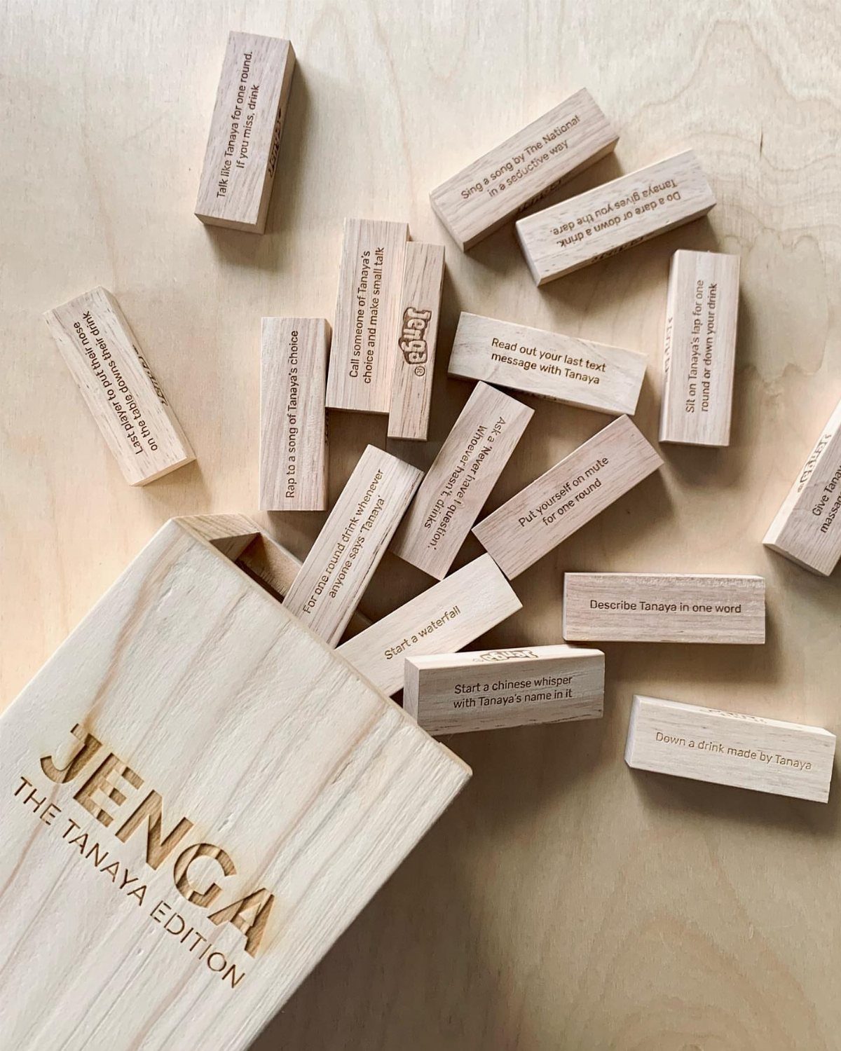 Customized Jenga blocks with text spilling from an engraved wooden storage box.
