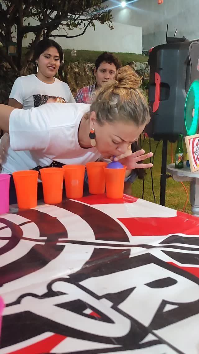Woman blowing a blue ping pong ball into orange plastic cups at a party.