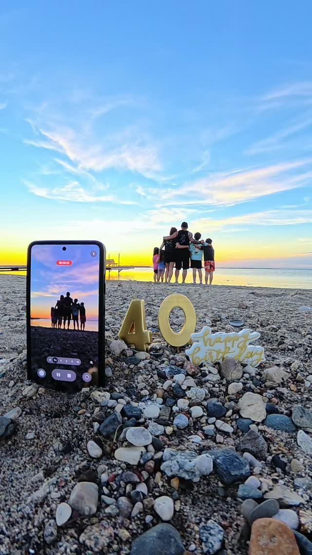 Smartphone and gold 40th birthday decorations on a beach with family at sunset