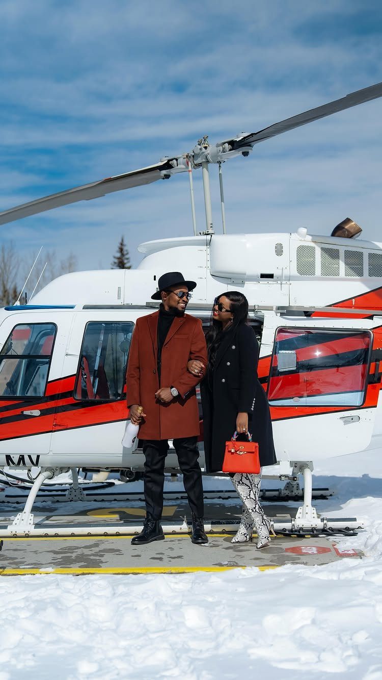 Couple posing in front of a white and red helicopter on snowy ground.
