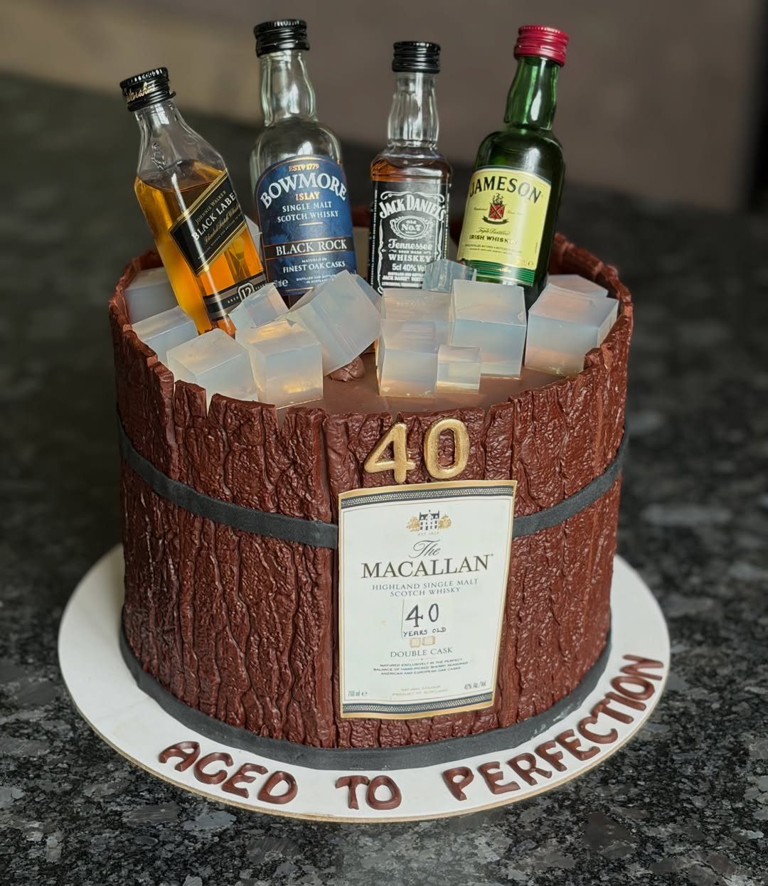 Whiskey barrel cake with miniature bottles and ice cubes for a 40th birthday.