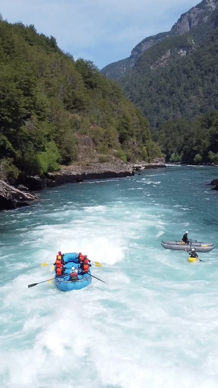 People white water rafting on a turquoise river between forested mountains