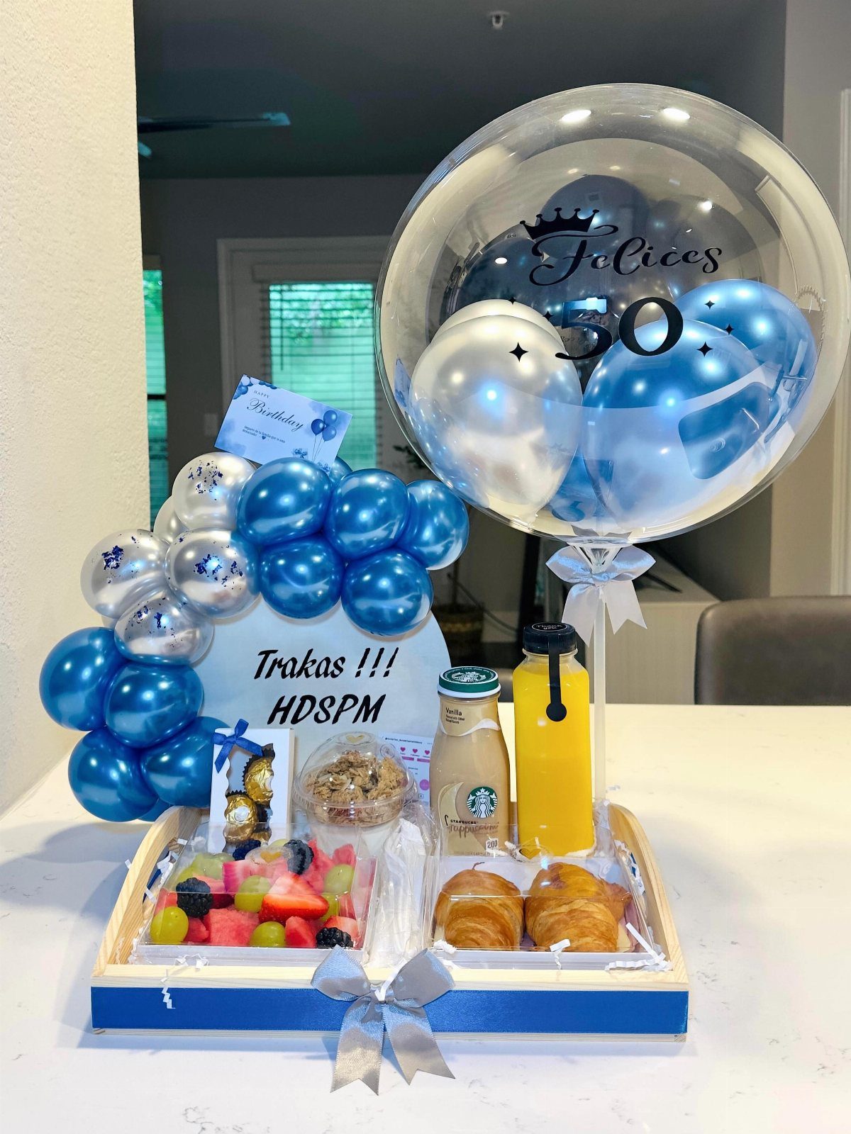 Birthday gift tray with food, drinks, blue balloons, and a 50th birthday balloon.